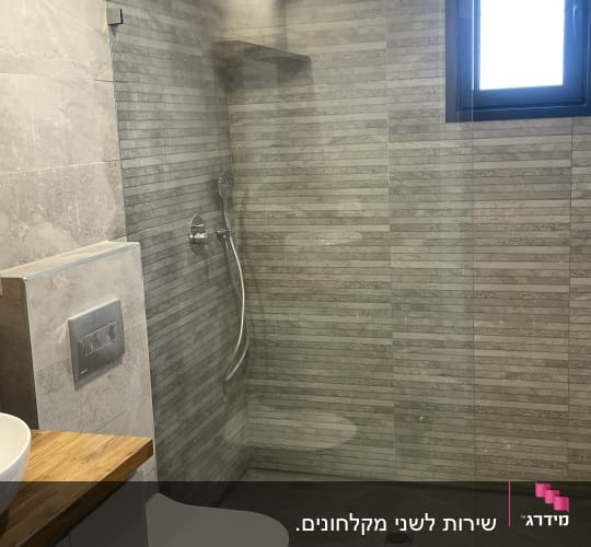מקלחת עם ראש מקלחת, קיר זכוכית ואריחים אפורים